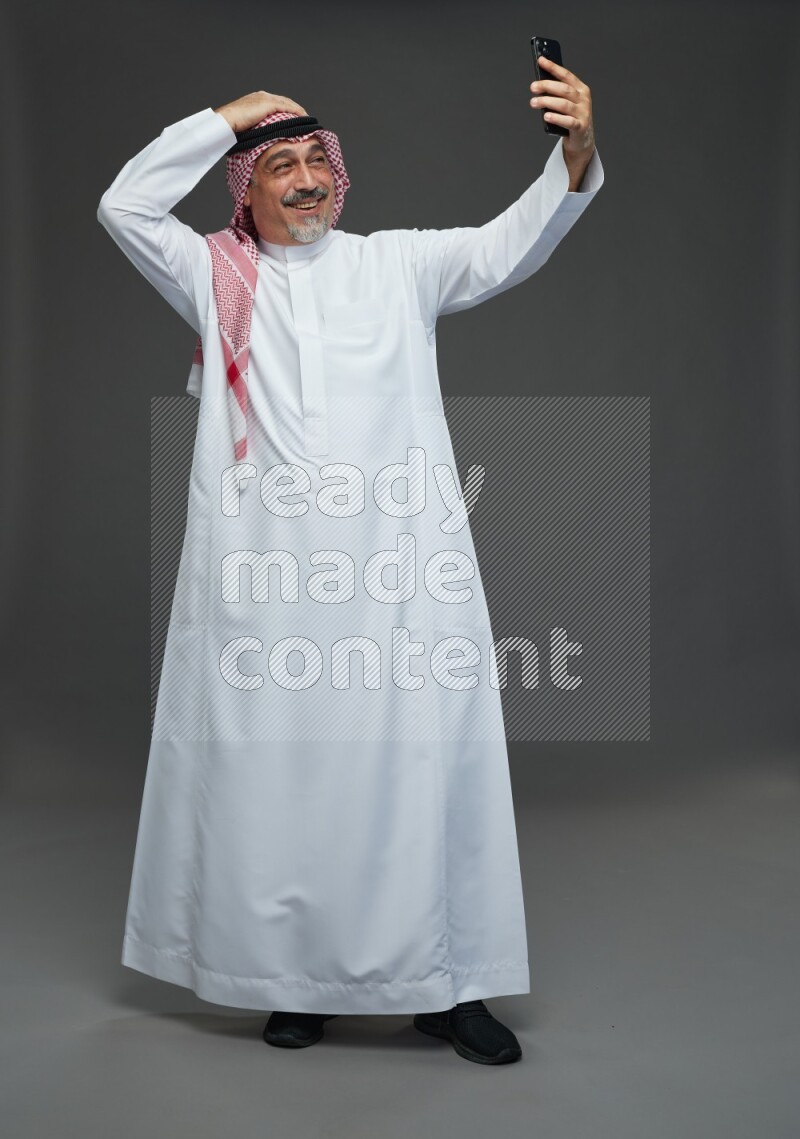 Saudi man with shomag Standing taking selfie on gray background