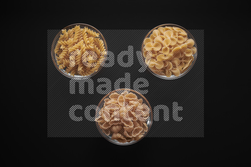 Different pasta types in glass bowls on black background