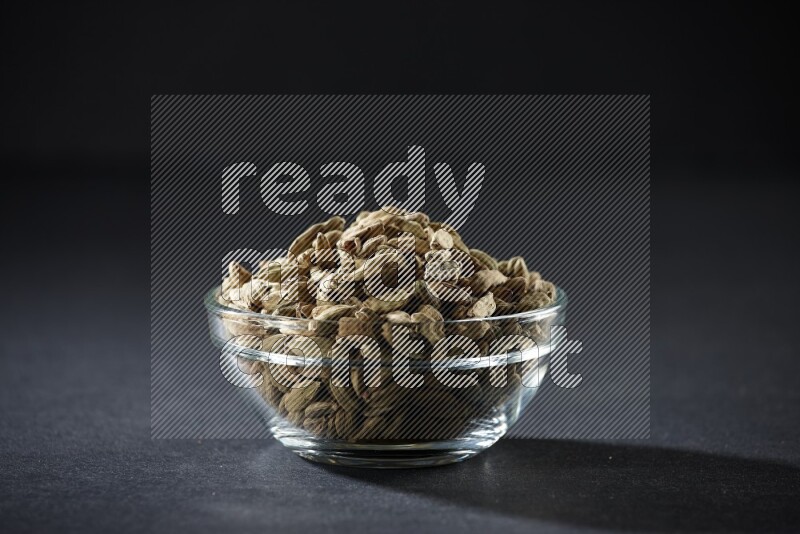 A glass bowl full of cardamom on black flooring