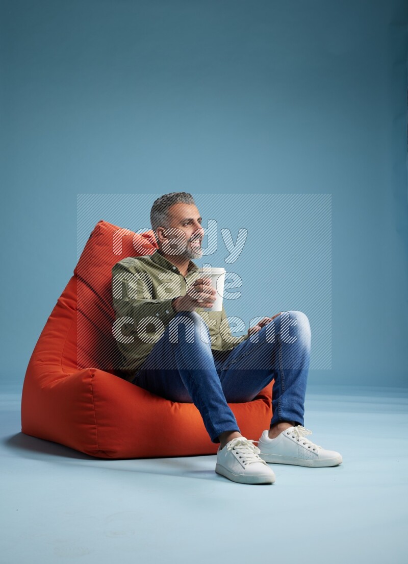 A man sitting on an orange beanbag and drinking coffee