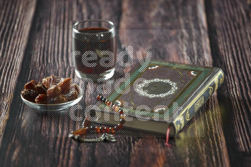 Quran with dates, prayer beads and different drinks all placed on wooden background