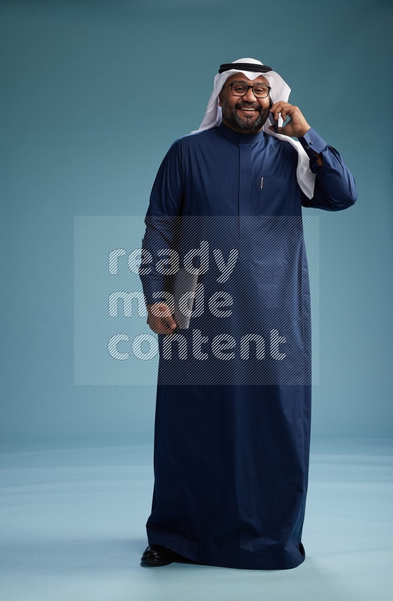 Saudi Man with shimag Standing talking on phone on blue background