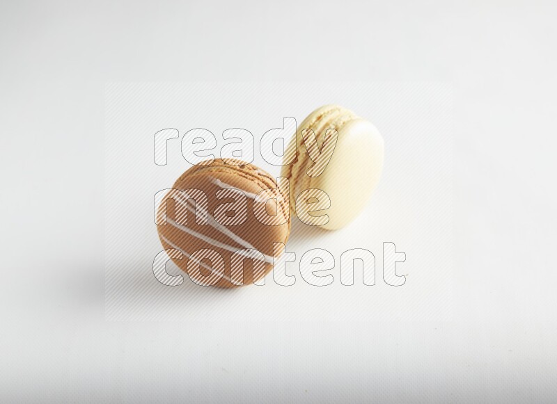 45º Shot of of two assorted Brown Irish Cream, and Yellow Vanilla macarons on white background