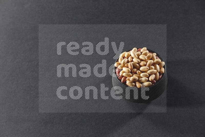 A black pottery bowl full of peeled peanuts on a black background in different angles