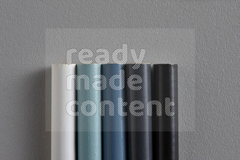 A collection of colored pencils arranged showcasing a gradient of white, grey and black hues on grey background