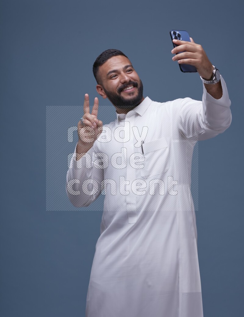 A Saudi man Taking A Selfie on Blue Background wearing Saudi Thob