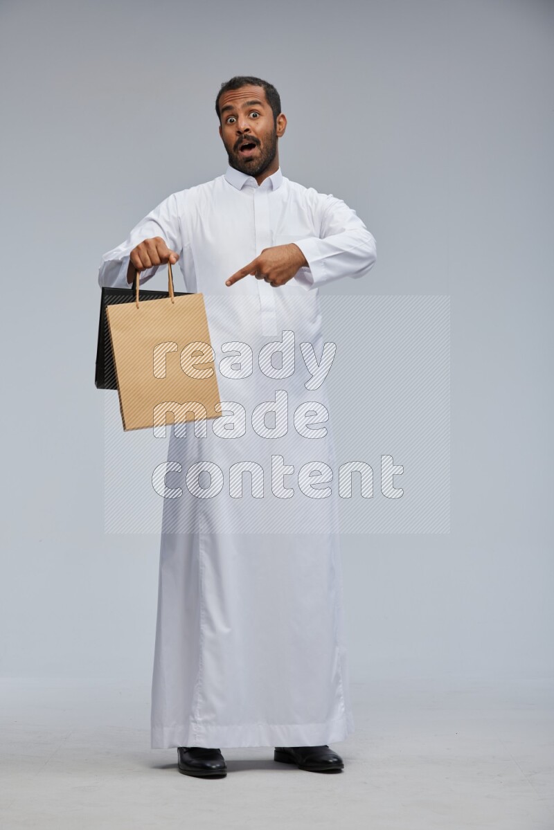 Saudi man Wearing thob standing holding shopping bag on Gray background
