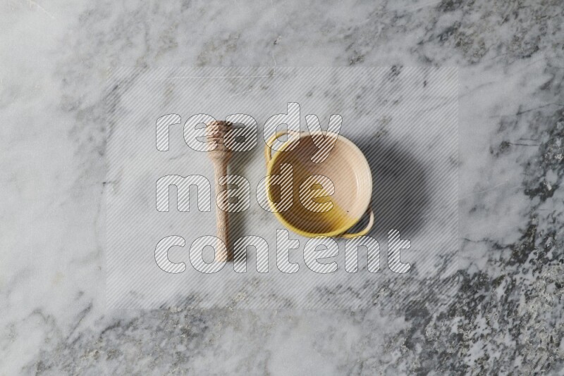 Multicolored pottery bowl with wooden honey dipper on the side on grey marble background