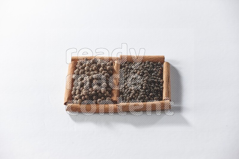 2 squares of cinnamon sticks full of black peppers and allspice on white flooring