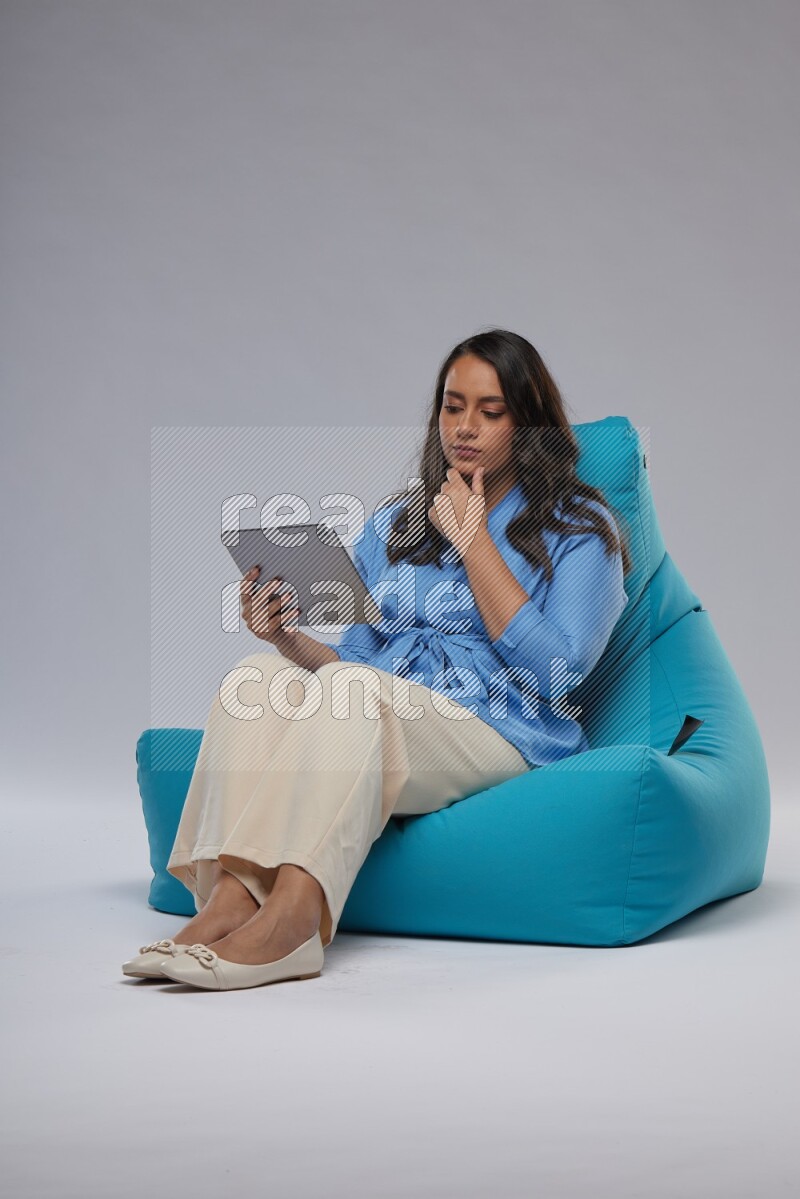 A woman sitting on a blue beanbag and working on tablet