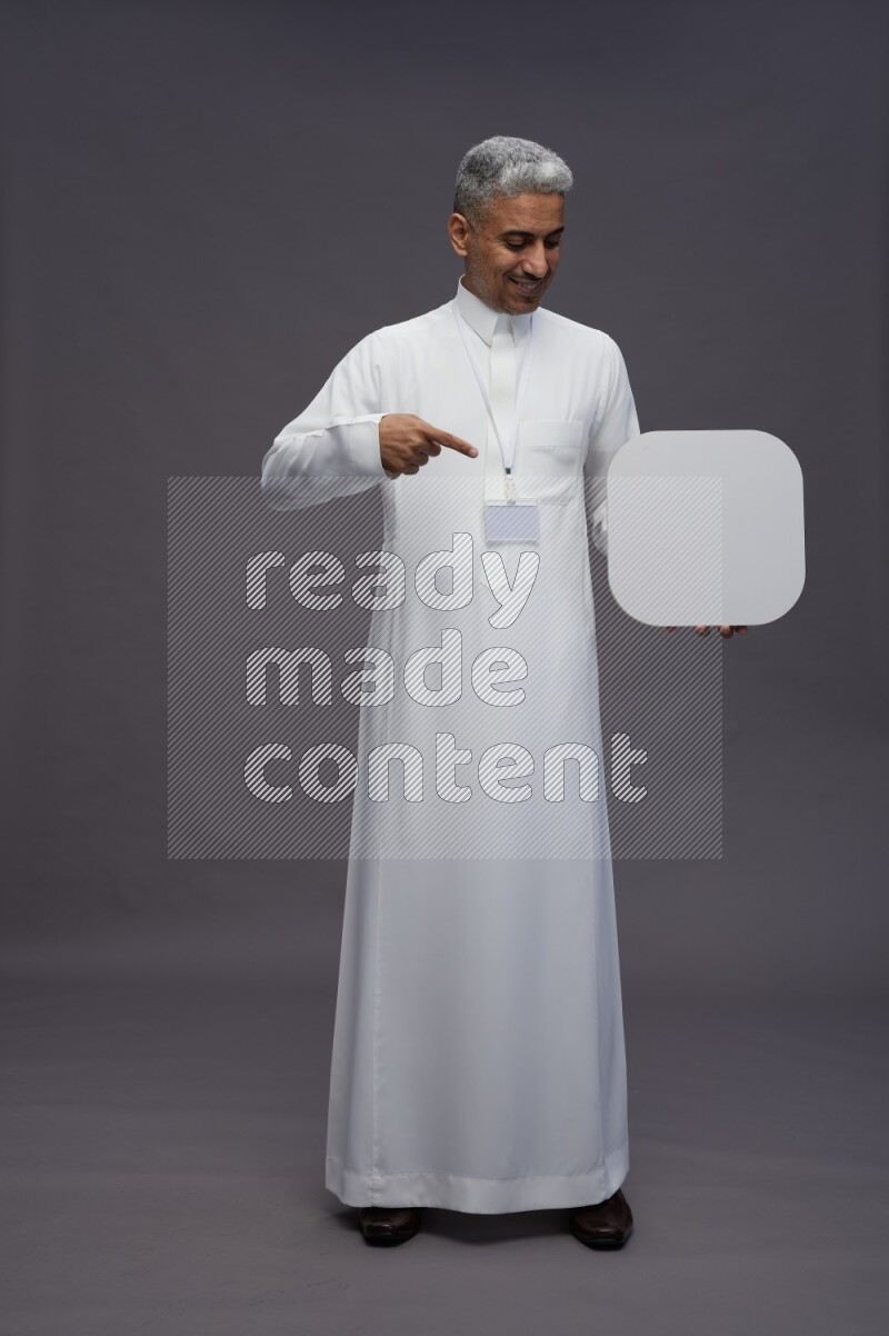 Saudi man wearing thob with neck strap employee badge standing holding social media sign on gray background