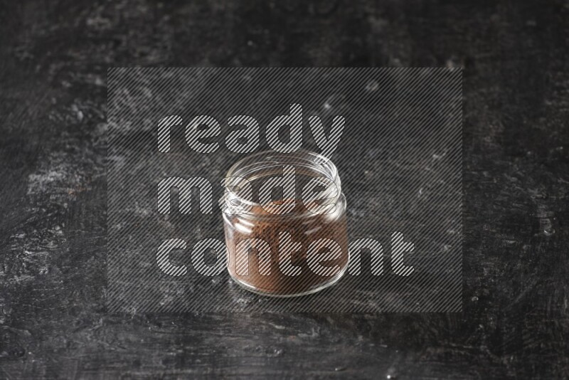 A glass jar full of cloves powder on a textured black flooring