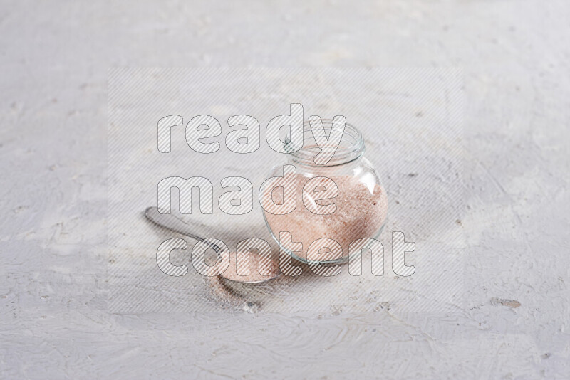 A glass jar full of fine himalayan salt on white background