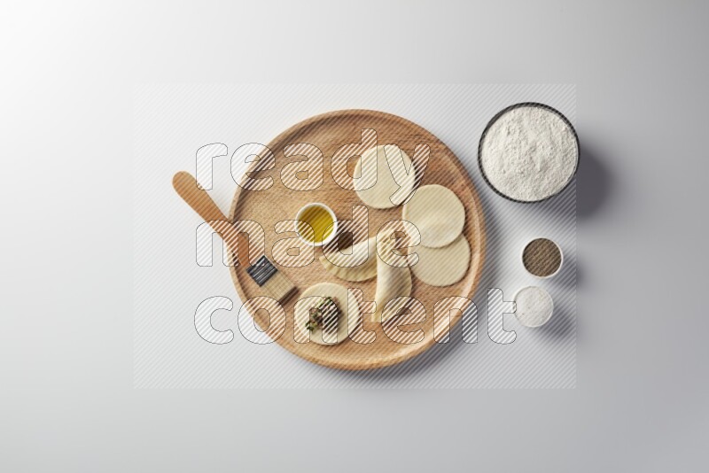 two closed sambosas and one open sambosa filled with meat while flour, salt, black pepper and oil with oil brush aside in a wooden dish on a white background