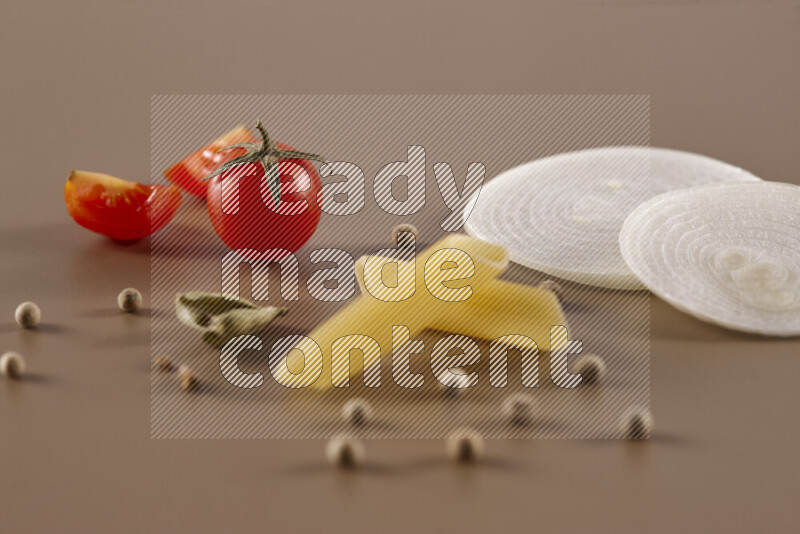 Raw pasta with different ingredients such as cherry tomatoes, garlic, onions, red chilis, black pepper, white pepper, bay laurel leaves, rosemary and cardamom on beige background