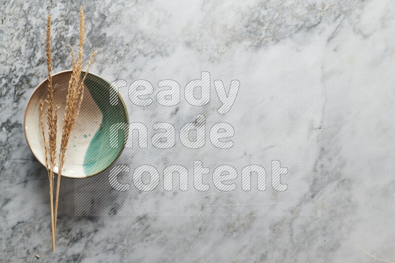 Wheat stalks on multicolored pottery plate on grey marble background