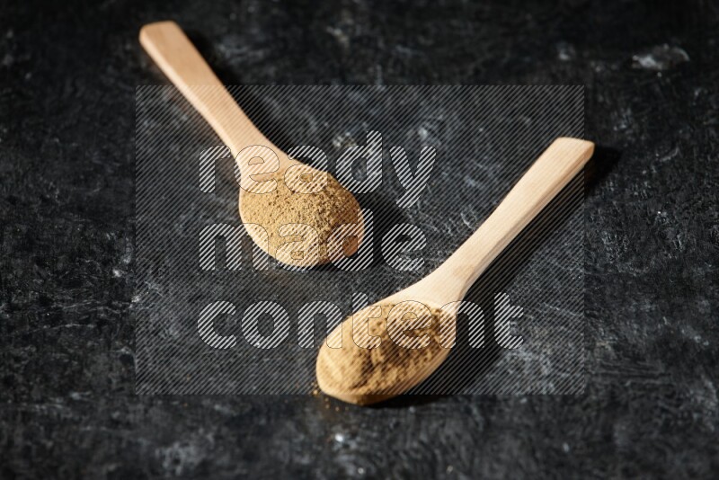 Wooden spoons full of allspice powder on a textured black flooring