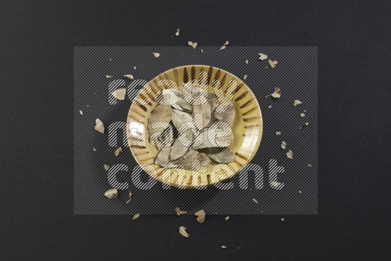 صحن فخاري متعدد الألوان ممتلئ بأوراق الغار المجففة على أرضية سوداء