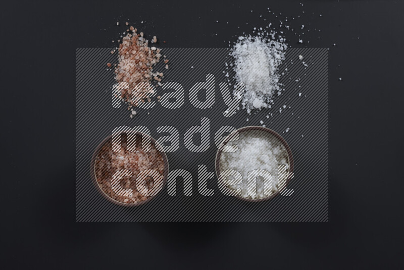 2 pottery bowls one is filled with himalayan salt and the other with white salt on black background
