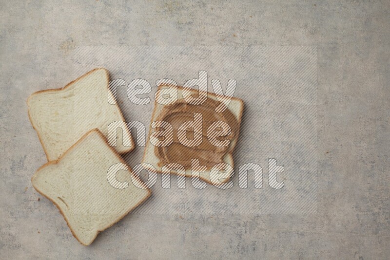 Creamy peanut butter on white toast and white toast slices on a light blue textured background