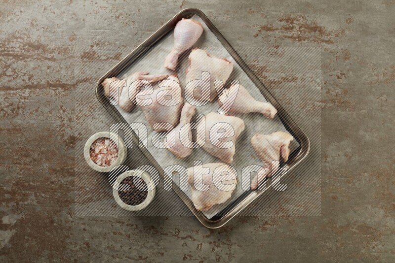Mixed fresh chicken pieces in an oven tray on a textured rustic background