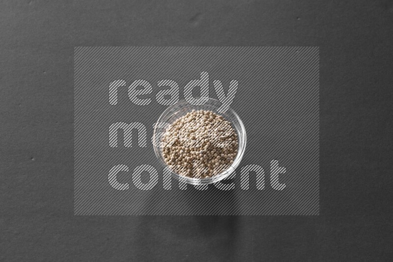 A glass bowl full of white peppers on black flooring