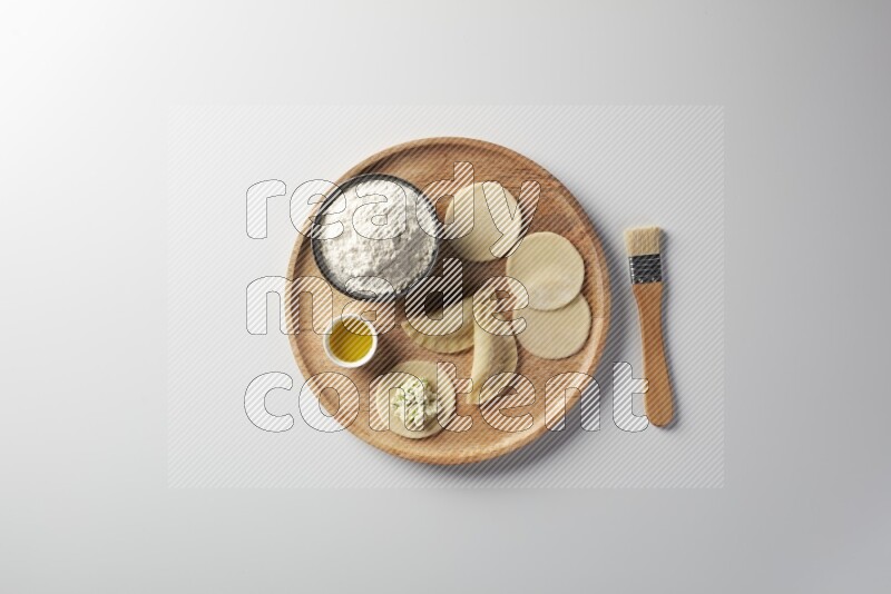 two closed sambosas and one open sambosa filled with cheese while flour, and oil with oil brush aside in a wooden dish on a white background
