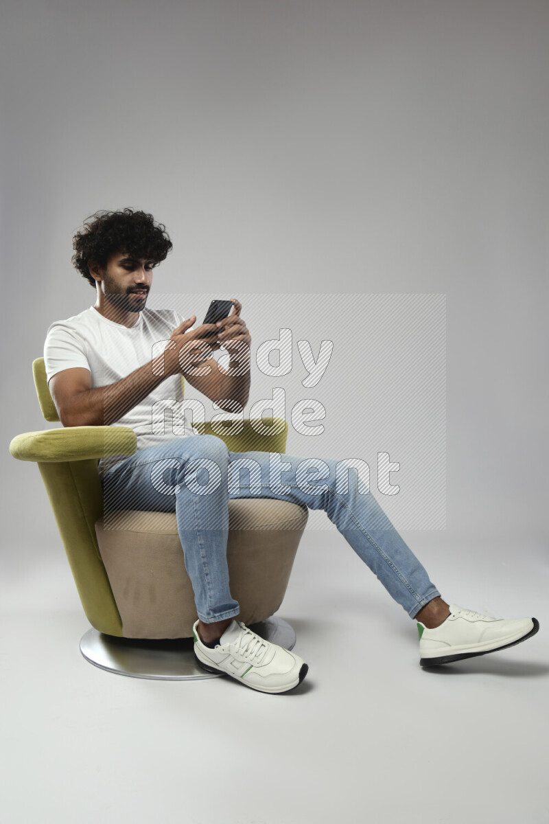 A man wearing casual sitting on a chair texting on the phone on white background