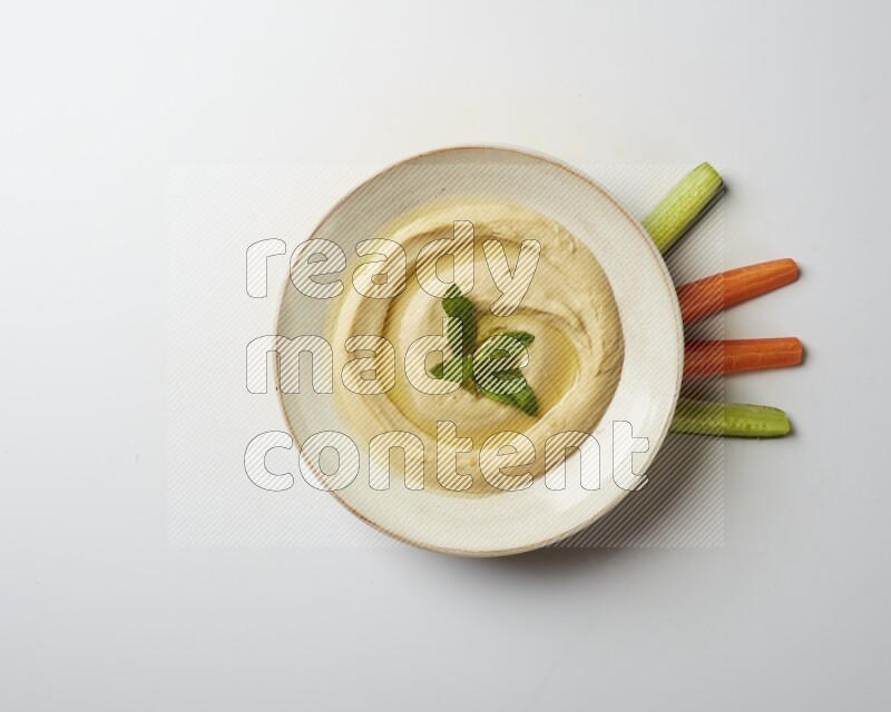 Hummus in a pottry plate garnished with mint  on a white background