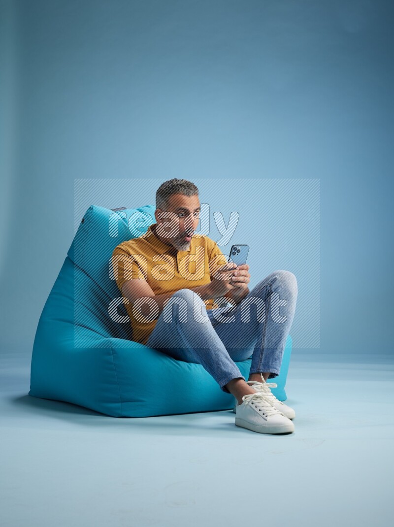 A man sitting on a blue beanbag and texting on phone