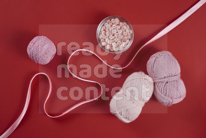 A pink and red collection of sewing and tailoring tools arranged on a red background