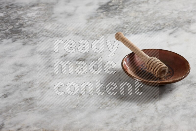 Decorative pottery plate with wooden honey dipper in it on grey marble background