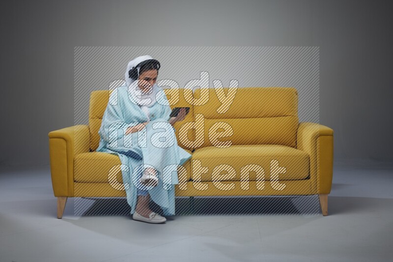 A Saudi woman sitting on a yellow Sofa Watching a Movie wearing Blue Abaya