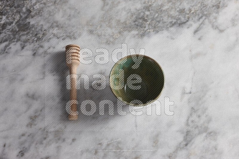Multicolored pottery bowl with wooden honey dipper on the side on grey marble background