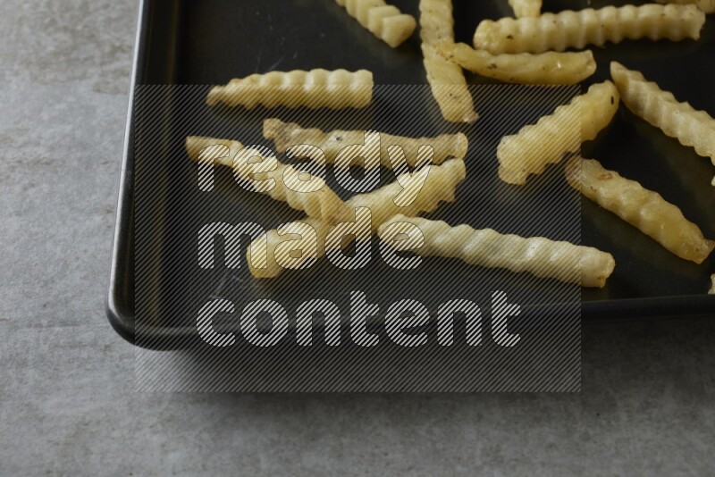 crinkle fries in a black stainless steel rectangle tray on grey textured counter top