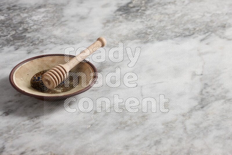 Decorative pottery plate with wooden honey dipper in it on grey marble background
