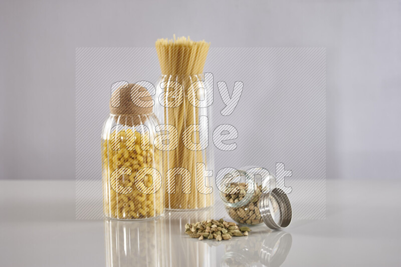 Raw pasta in glass jars with cardamom on light grey background