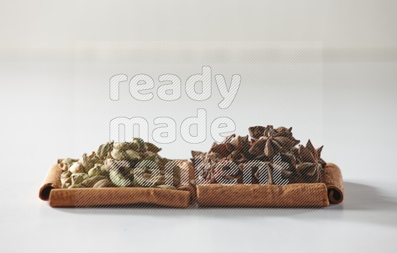 مربعان من أعواد القرفة ممتلئان باليانسون النجمي وحبوب الهيل علي خلفية بيضاء