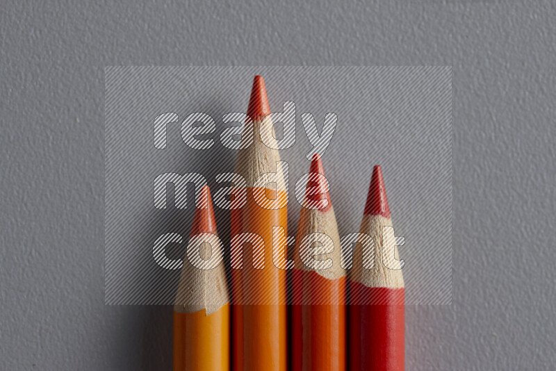 A collection of colored pencils arranged showcasing a gradient of orange hues on grey background