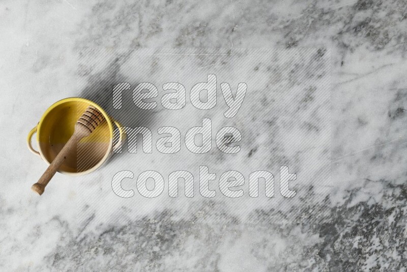 Multicolored pottery bowl with wooden honey dipper in it on grey marble background