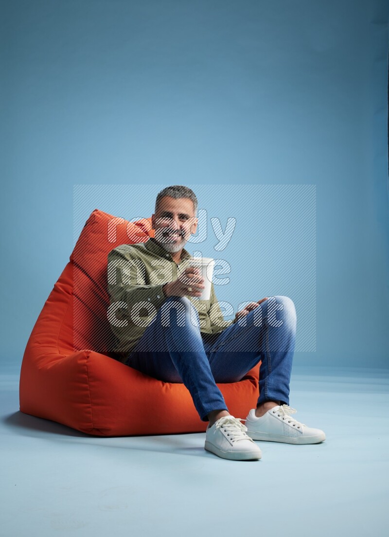 A man sitting on an orange beanbag and drinking coffee