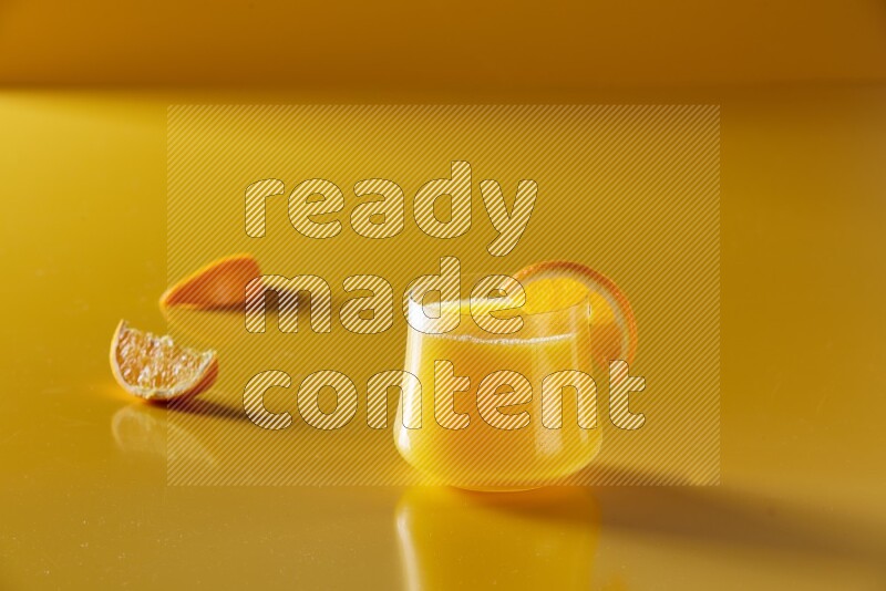 glass of orange juice with orange slice on yellow background