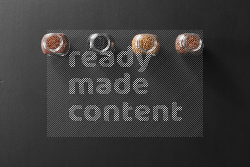 4 glass spice jars full of black seeds, mustard seeds, flax and garden cress on black flooring