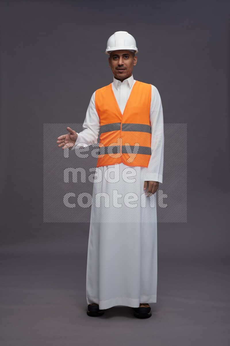 Saudi man wearing thob with engineer vest standing interacting with the camera on gray background