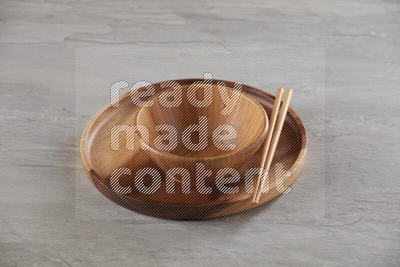 brown wood round bowl on top of brown wood round plate and wood chopsticks, on grey textured countertop