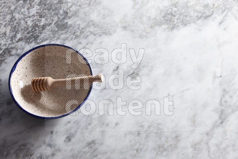 Multicolored pottery bowl with wooden honey dipper in it on grey marble background