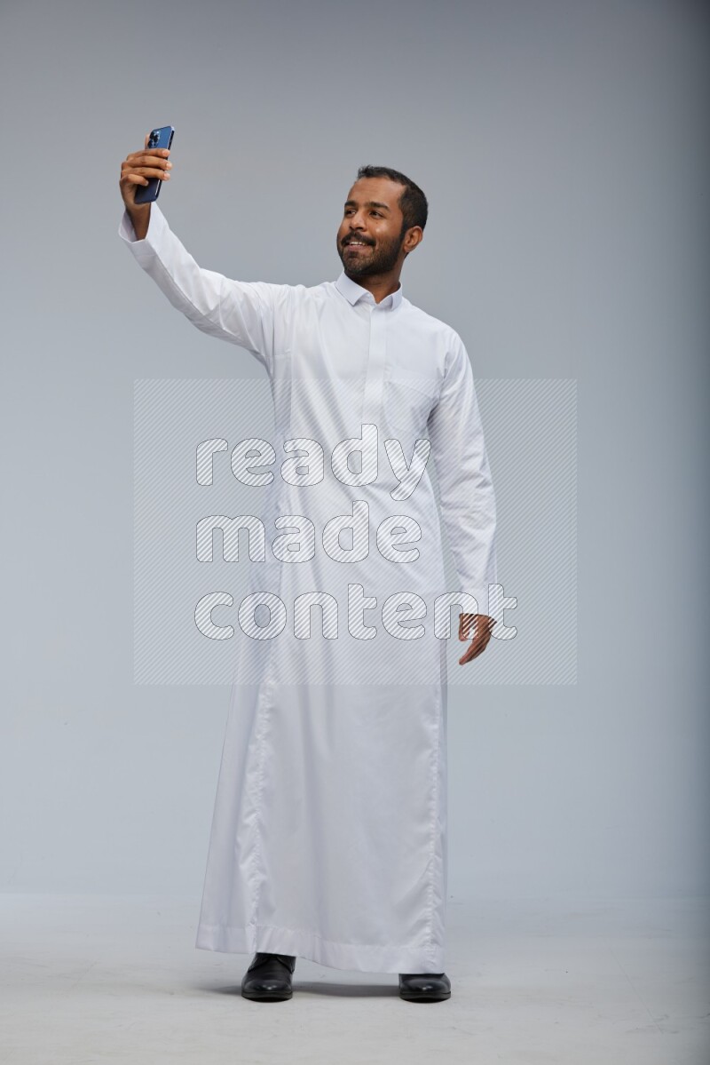 Saudi man wearing Thob standing taking selfie on Gray background