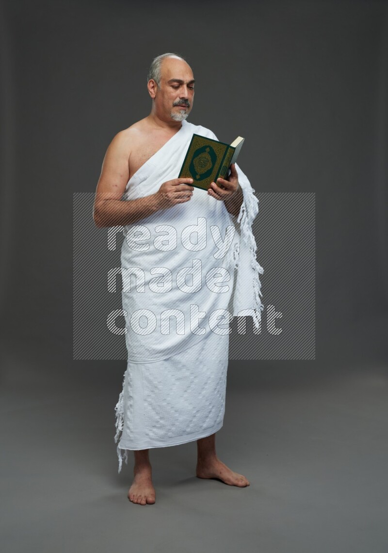 A man wearing Ehram Standing reading quran on gray background