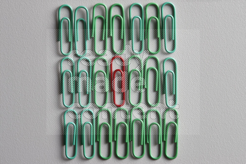 A bunch of green paper clips with a different colored paper clip in the center on grey background