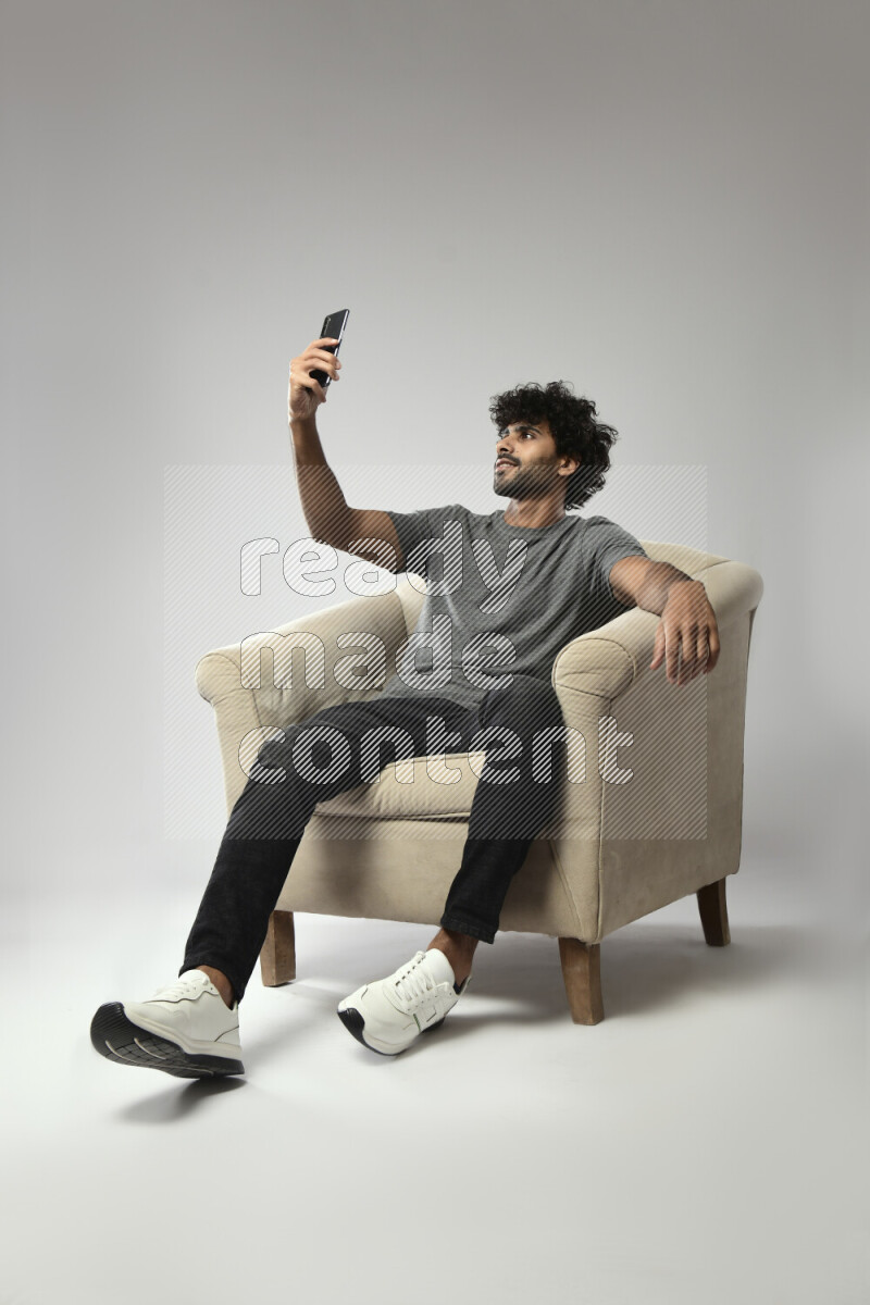 A man wearing casual sitting on a chair taking a selfie on white background